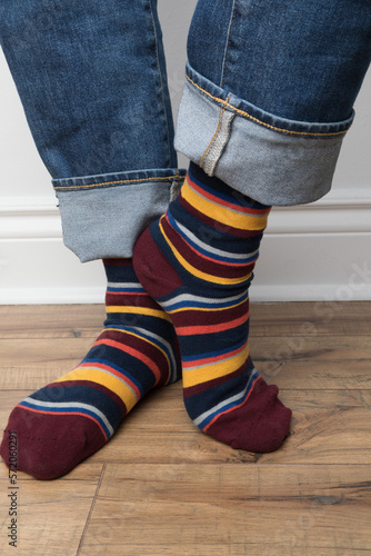 Product photo of men's fancy socks. The socks are burgundy with colorful stripes. The man is wearing jeans. 