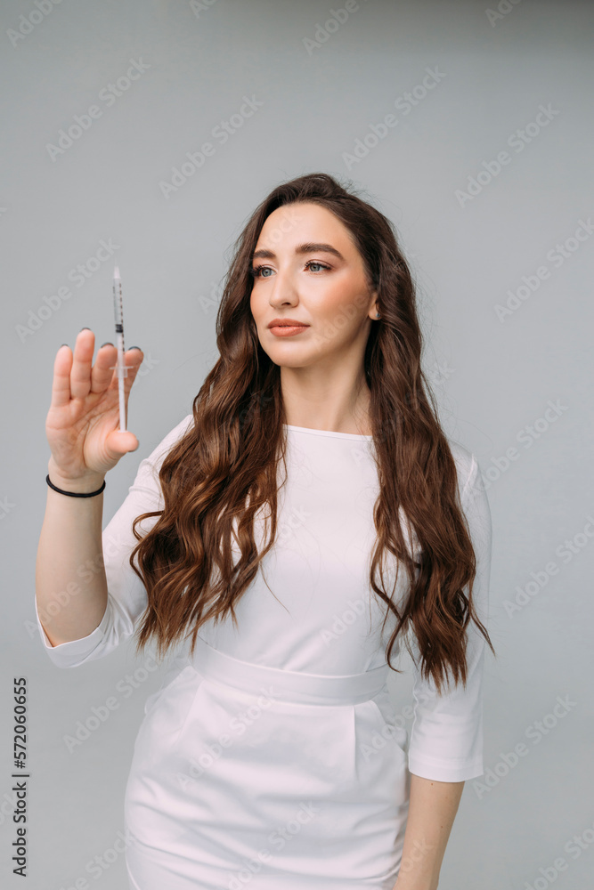 Obraz premium young woman doctor in a white coat holds an insulin syringe in her hand. Girl cosmetologist preparing to make an injection of hyaluronic acid in a cosmetology clinic
