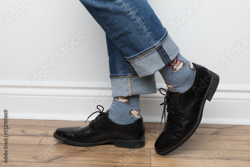 Product photos of men's footwear. Close up photo of a man's foot and legs. He is wearing blue jeans, colorful blue socks and black dress shoes. 