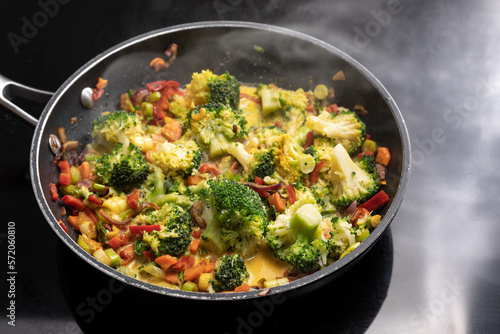 Vegetarian curry with broccoli and other vegetables in a steaming frying pan on a black stovetop, Asian cooking concept, copy space, selected focus