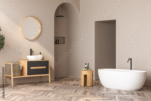 Interior of modern bathroom with beige walls, wooden floor, bathtub, plants, shower, white sink standing on wooden countertop and a oval mirror hanging above it. 3d rendering