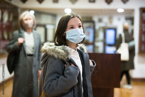 Portrait of inquisitive preteen girl wearing protective face mask visiting exposition in historical museum during coronavirus pandemic