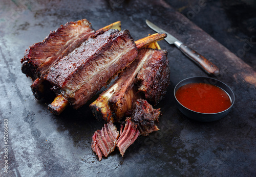 Traditional barbecue burnt chuck short beef ribs marinated with spicy rub and served with a hot chili sauce as close-up on a rustic board photo