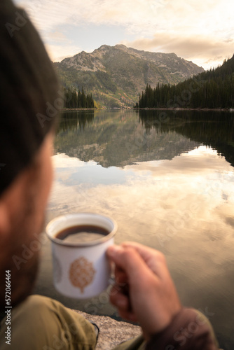 Hiker drinking coffee at alpine lake in Montana on a backpacking trip