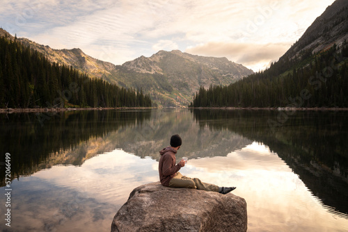 Hiker drinking coffee at alpine lake in Montana on a backpacking trip