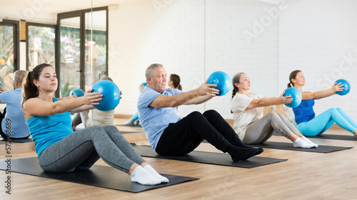 Sportive young woman doing pilates exercises with ball in gym area during workout session. Persons engaging in pilates in fitness room