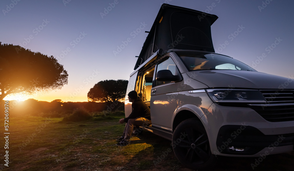 man sitting with digital device at his Transporter Camping Van bus at the California Ocean in the coastal Nature - digital nomades concept