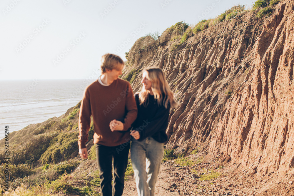couple walking on the path on the bluff over the ocean on beach holding hands and smiling