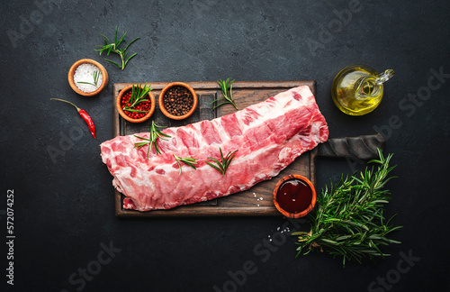 Fotografiet Raw pork ribs with rosemary and spices on rustic wooden cutting board prepared f