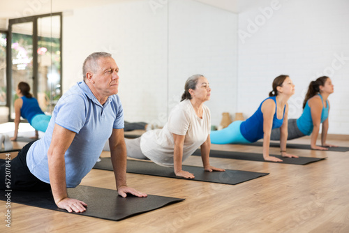 People of different ages performing cobra exercise during group Pilates workout. Active lifestyle and wellness concept