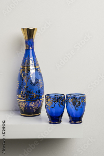 A transparent blue glass bottle with gold decorations and glasses of the same set