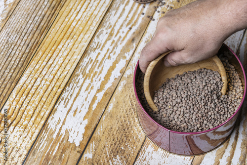 A hand with a wooden bowl scooping dried lentils out of a purple colored tin container photo