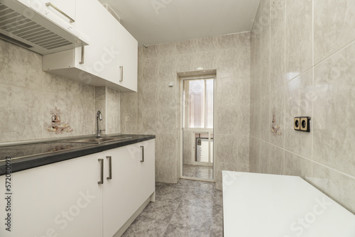 Kitchen equipped along a wall with white cabinets with gray countertops with access to a terrace with white aluminum windows and stoneware tiled floors and walls