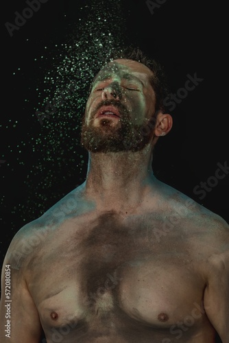 portrait of shirtless male model with beard with bright neon green, blue and black body paint. chest and shoulders bare skin headshot. body art, isolated studio shoot with black background