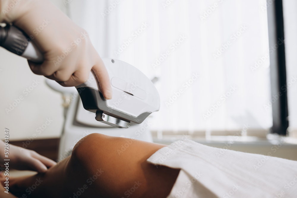 Fototapeta premium Beautician removes hair on beautiful female legs using a laser. Hair removal on the legs, laser procedure at clinic