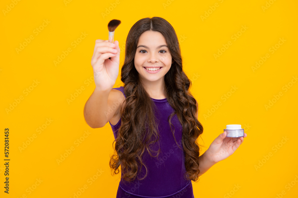 Beauty, make up and kids cosmetics. Teenage child girl with brush applying blush to face isolated on wellow background. Happy girl face, positive and smiling emotions. Beauty, make up and kids cosmetics. Teenage child girl with brush applying blush to face isolated on wellow background. Happy girl face, positive and smiling emotions.