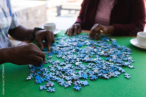 Mid section of african american senior couple solving jigsaw puzzle at home