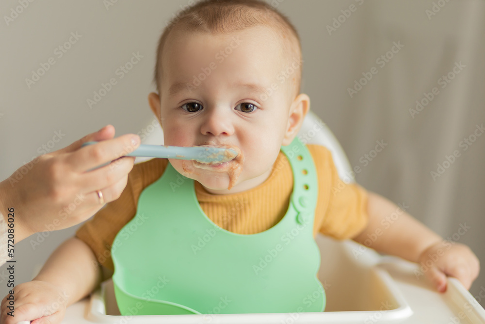 baby 1 year old eats baby food from a spoon sitting at the table, the first complementary foods and healthy food for small children. baby 1 year old eats baby food from a spoon sitting at the table, the first complementary foods and healthy food for small children.