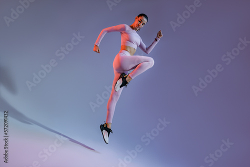 Athletic active woman jumping on studio background with colored filter. Dynamic movement