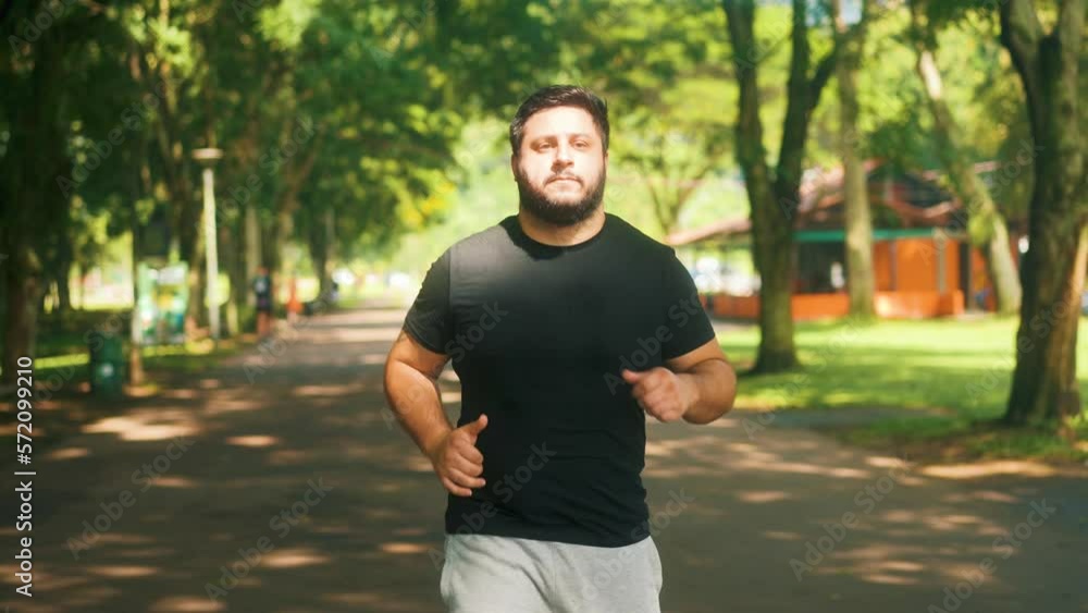 Front view following man jogging at the park on a sunny summer day slow motion Front view following man jogging at the park on a sunny summer day slow motion