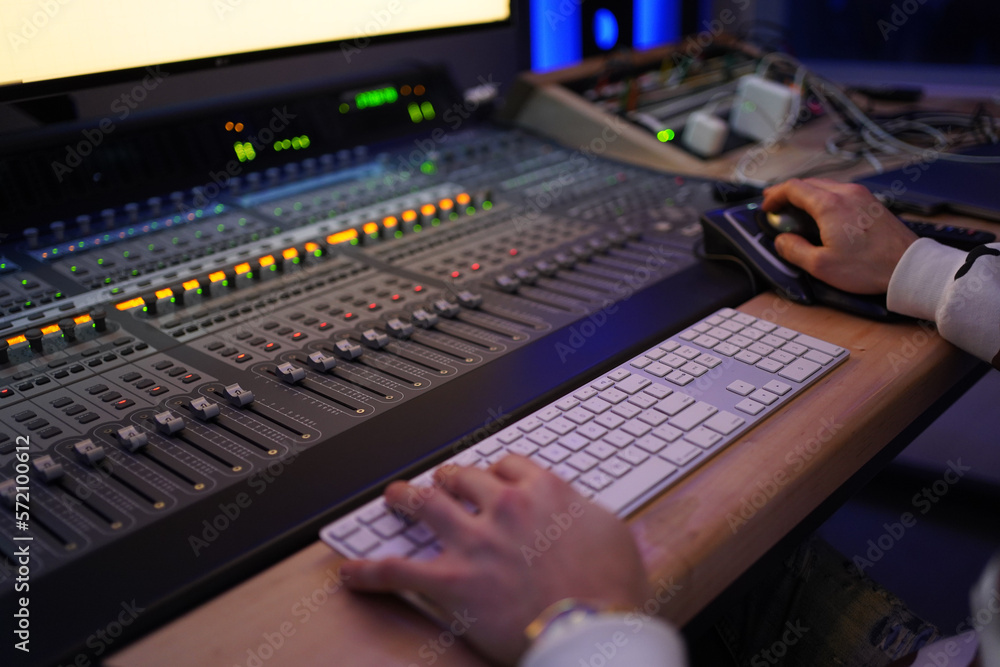 Producer / Sound Engineer creating and editing a song on an audio console with a screen displaying the track on top. Shot in an indoor music studio with blue and purple ambient lighting. Producer / Sound Engineer creating and editing a song on an audio console with a screen displaying the track on top. Shot in an indoor music studio with blue and purple ambient lighting.