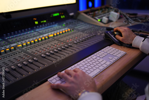 Producer / Sound Engineer creating and editing a song on an audio console with a screen displaying the track on top. Shot in an indoor music studio with blue and purple ambient lighting.