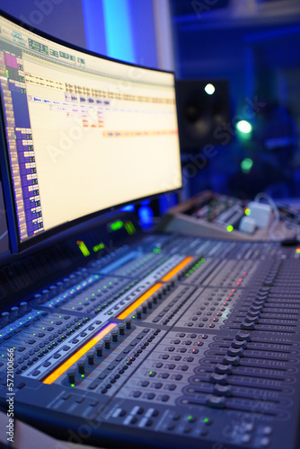 Producer / Sound Engineer creating and editing a song on an audio console with a screen displaying the track on top. Shot in an indoor music studio with blue and purple ambient lighting.