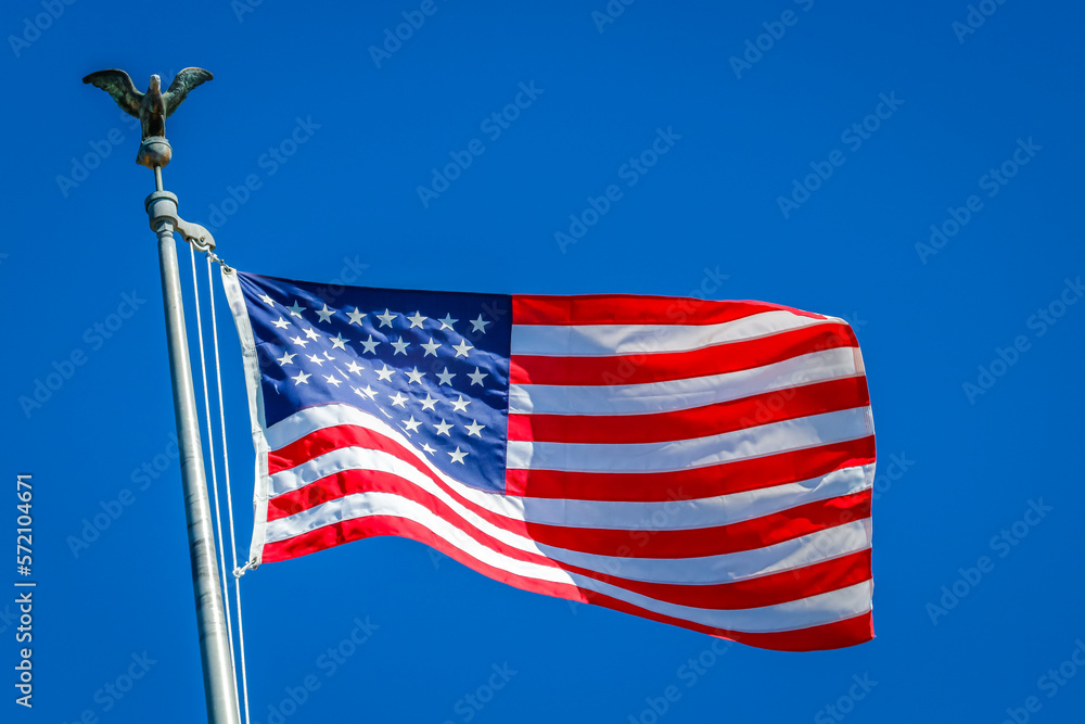 American flag waving on pole with eagle and bright colors against blue sky
