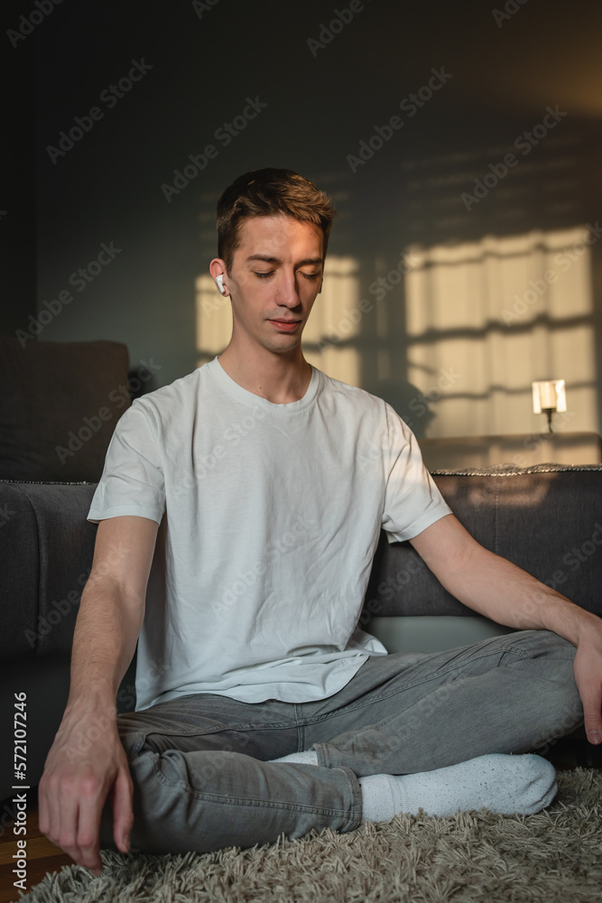 A young guy is sitting on the floor and meditating while listening to music A young guy is sitting on the floor and meditating while listening to music