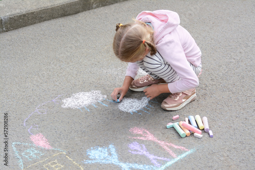 Little child drawing white clouds with chalk on asphalt