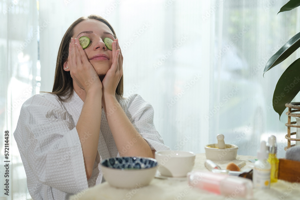 Beautiful young woman putting slices of cucumber on her eyes and while doing beauty treatment at home.Beauty routine, self care. Beautiful young woman putting slices of cucumber on her eyes and while doing beauty treatment at home.Beauty routine, self care.