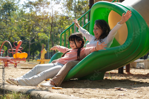 Overjoyed senior grandmother and little granddaughter having fun on colorful slide. Family relations and weekend activities concept.