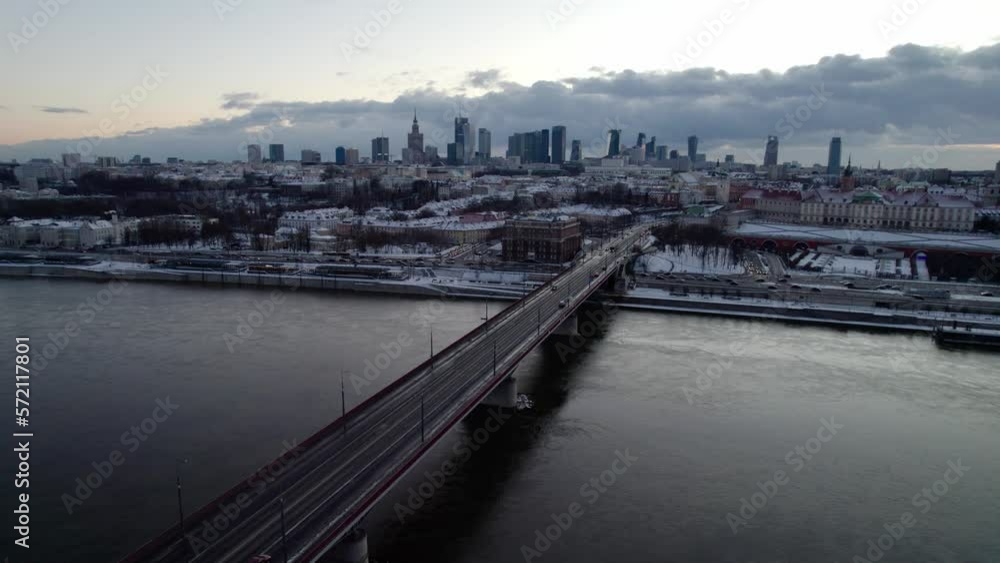 Drone shot showing Vistula River and driving cars on bridge in direction Warsaw during sunset time in winter - Skyline with high-rise buildings in background Drone shot showing Vistula River and driving cars on bridge in direction Warsaw during sunset time in winter - Skyline with high-rise buildings in background