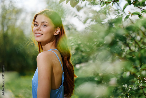Woman smile with teeth in profile happiness in nature in the summer near a green tree in the garden of the park in a blue dress  the concept of women s health and beauty with nature sunset