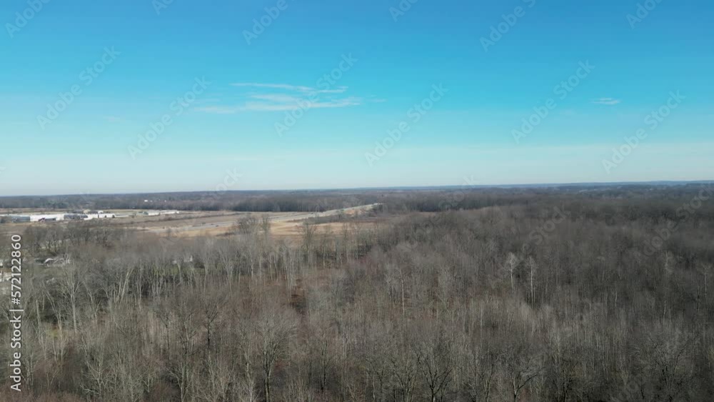 An aerial shot of trees that are bare in the middle of winter with blue skies and a highway off in the distant. An aerial shot of trees that are bare in the middle of winter with blue skies and a highway off in the distant.