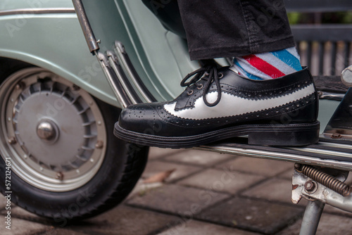 These hand-made black-and-white wingtip shoes with loafers sole made from genuine leather are being worn to hang out with an old green Vespa 
