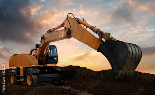 wheeled excavator at work digging soil during sunset.