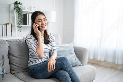 Asian beautiful woman sit on sofa and talk on mobile phone in house. 
