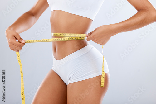 Weightloss, health and woman with measuring tape in a studio for her diet, exercise or wellness. Fitness, body and healthy slim female model checking the measurement of her waist by a gray background photo