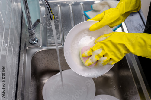Housemaid with yellow rubber gloves washing dish in kitchen sink, Hands Concept