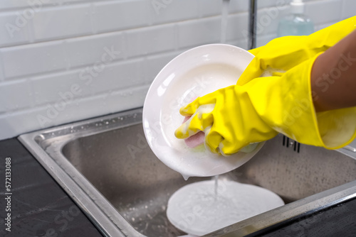 Close up housemaid with yellow rubber gloves washing dish in sink , Hands Concept