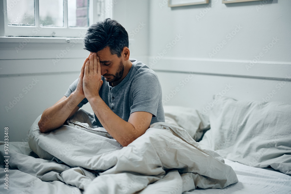 Distraught man with hands clasped sitting on bed in morning. Distraught man with hands clasped sitting on bed in morning.