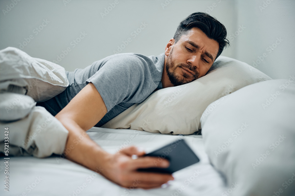 Fototapeta premium Sleepy man turns off the alarm on his phone in morning in bed.