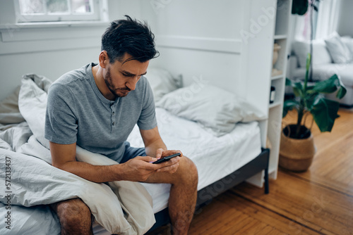 Mid adult man text messaging on cell phone after waking up in morning at home.