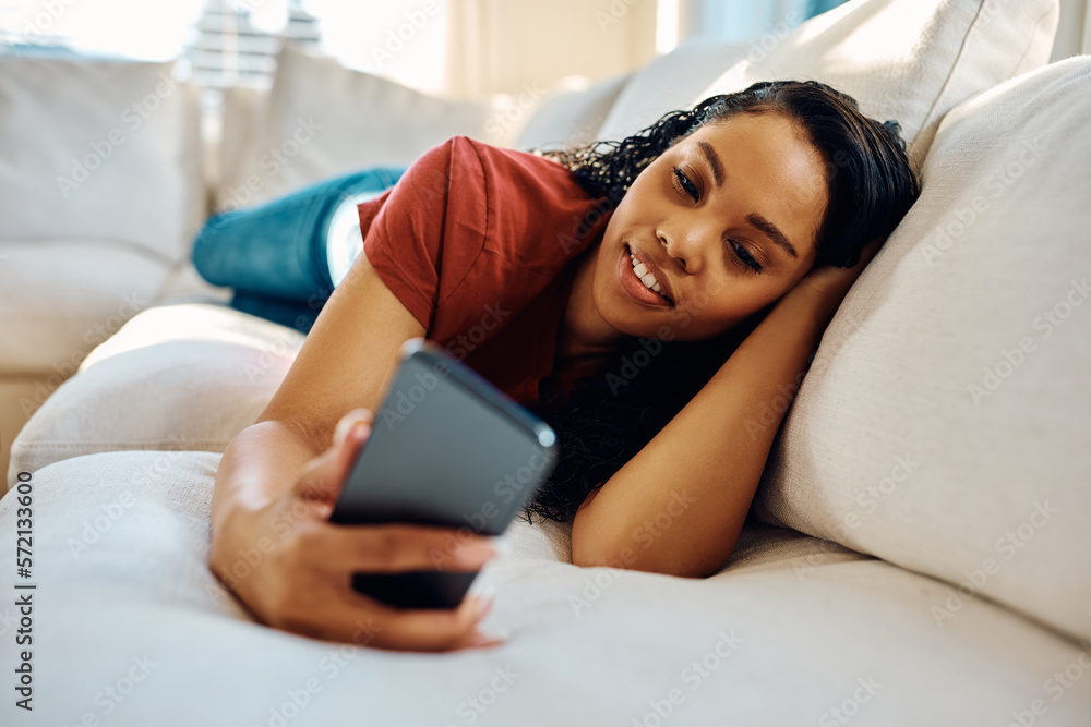 Young African American woman using smart phone while relaxing on sofa. Young African American woman using smart phone while relaxing on sofa.