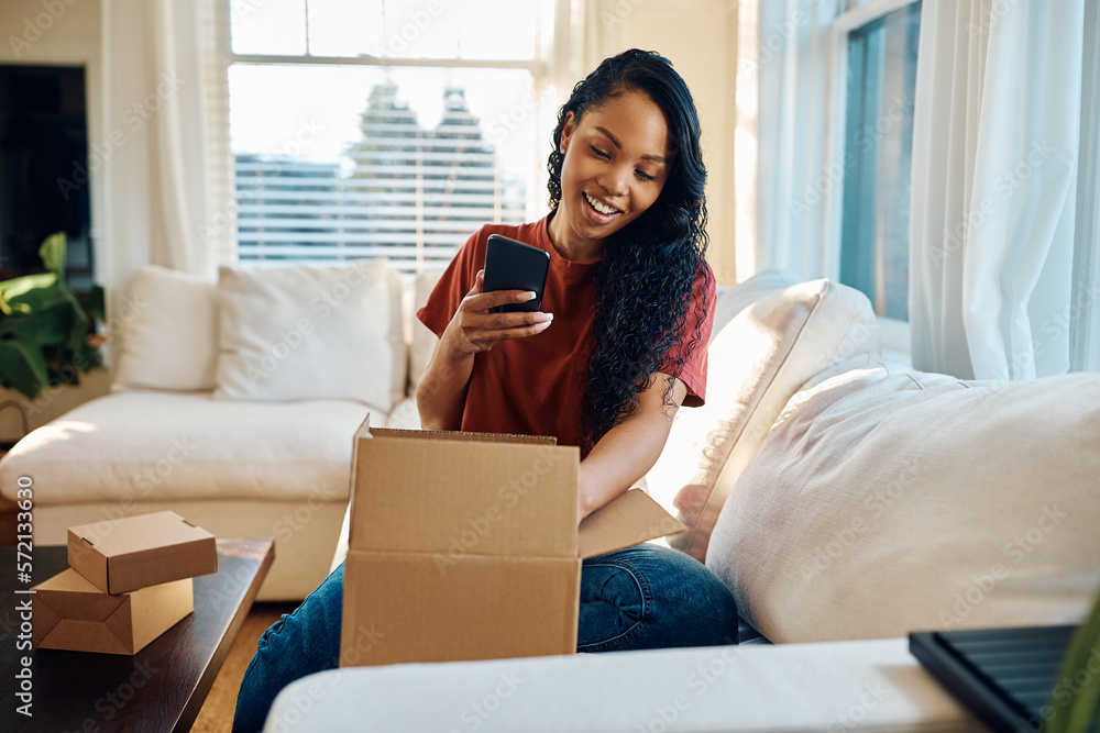 Happy black woman using cell phone while unpacking home delivered package. Happy black woman using cell phone while unpacking home delivered package.