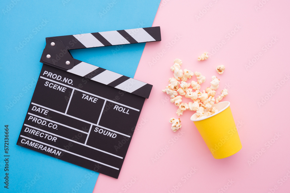 Cinema clapperboard and popcorn in paper bag on pink blue colorful background - Movie cinema entertainment concept.