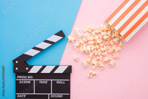 Foto Cinema clapperboard and popcorn in paper bag on pink blue colorful background -