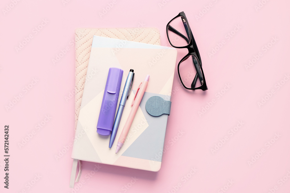 Notebooks, pens, marker and eyeglasses on pink background Notebooks, pens, marker and eyeglasses on pink background