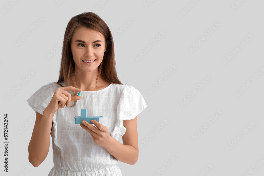 Beautiful woman with container of vitamin supplements on grey background Beautiful woman with container of vitamin supplements on grey background